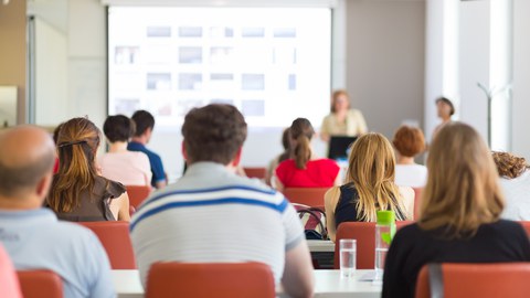 Das Bild zeigt eine Gruppe von Zuhörern in einem Seminarraum während einer Präsentation.