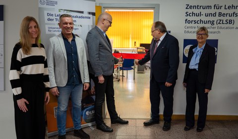 Gruppenbild mit 5 Personen, während zwei Personen in der Mitte symbolträchtig ein rotes Band durchschneiden.