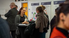 Zwei Frauen im Gespräch an einem Stehtisch, drum herum herrscht buntes Treiben.