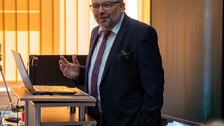 Mann hält Vortrag und steht dabei an einem Pult