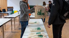 Student übergibt Campusbeutel einem anderen Studenten