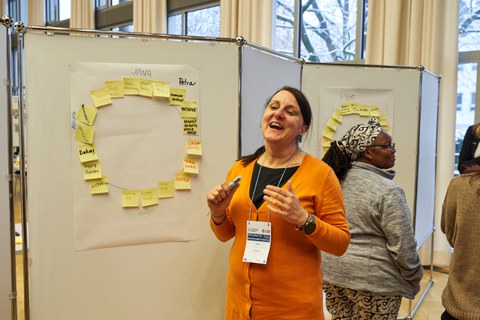 Eine Frau erklärt etwas an einem Whiteboard, an welchem ein Kreis aus Post-its hängt.