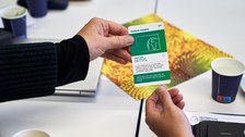 Zwei Hände halten gleichzeitig einen Spielkarte, auf der in englischer Sprache etwas zu Nachhaltigkeit erklärt wird.