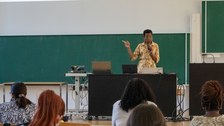 Frau hält Vortrag mit Mikrofon vor einer Tafel