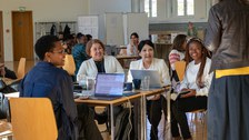 Eine Gruppe von erwachsenen Personen an einem Tisch, die einem Vortrag zuhören.