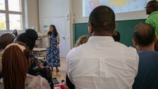 Frau gibt Vortrag vor einer Gruppe Menschen mit verschiedenen Nationalitäten.