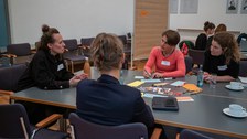 Gruppe von vier Frauen sitzt an einem Tisch und diskutiert miteinander.