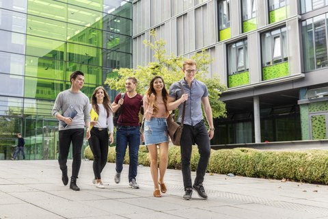 Foto von fünf Studierenden, die den Andreas-Pfitzmann-Bau verlassen und sich dabei unterhalten. 