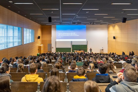 Eine Vortragende steht vor einem komplett gefüllter Hörsaal