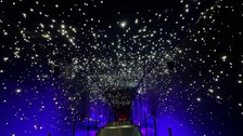 Ein schmaler Gang in einem dunklen Raum mit ganz vielen sternähnlichen LEDs an der Decke. 