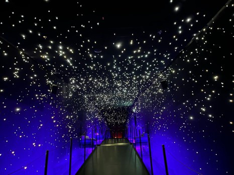 Ein schmaler Gang in einem dunklen Raum mit ganz vielen sternähnlichen LEDs an der Decke. 