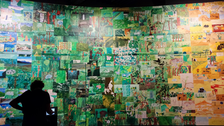 Foto zeigt eine große Wand voller selbst gemalter Bilder - in grün und gelb gehalten.