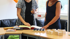 Zwei Kolleginnen erkunden inklusive Materialien wie beispielsweise ein Kinderbuch zu Diversity bzw. ein Fühlpärchen-Spiel.