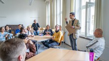 Ein Mann erklärt an Tischen sitzenden Personen etwas.