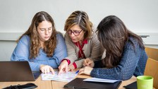 Drei Personen sitzen über ein Blatt Papier gebeugt.