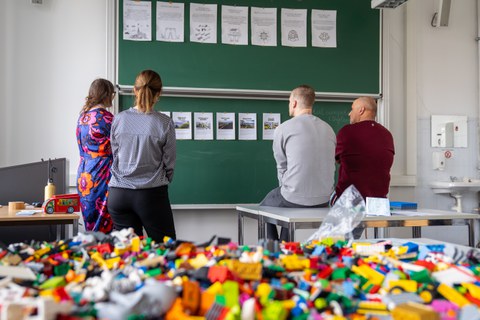 4 Personen schauen sich Ausdrucke auf einer Tafel an.