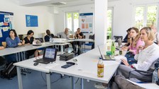 Das Foto zeigt einen Raum mit ca. 10 Personen während eines Workshops. Dabei sind die Zuhörer:innen von vorne fotografiert.