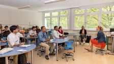 Das Foto zeigt ein Klassenzimmer, in dem erwachsene Personen sitzen und gespannt zuhören. 