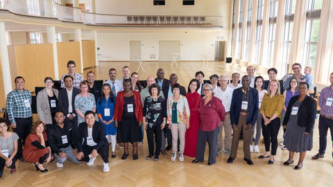 Das Foto zeigt eine Gruppe von ca. 30 Personen unterschiedlicher Herkunft in einem Saal, die sich zum einen Gruppenbild aufgestellt haben. 