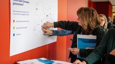 Foto: Zwei Personen betrachten ein Plakat an einer roten Wand.