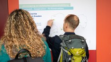 Foto: Eine Person betrachtet ein Plakat an einer roten Wand.