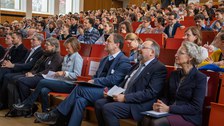 Foto: Personen in einem vollbesetzten Hörsaal blicken zur Bühne.