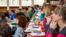 Foto: Personen in einem vollbesetzten Hörsaal blicken zur Bühne.