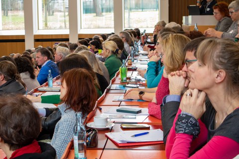 Foto: Personen in einem vollbesetzten Hörsaal blicken zur Bühne.