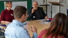 Foto: Mehrere Personen sitzen um einen Tisch und unterhalten sich.