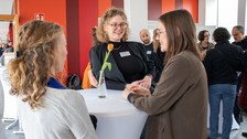 Foto: Mehrere Personen stehen um einen Tisch und unterhalten sich.
