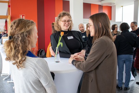 Foto: Mehrere Personen stehen um einen Tisch und unterhalten sich.
