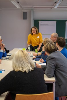 Foto: Mehrere Personen sitzen um einen Tisch und unterhalten sich.