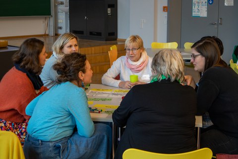 Foto: Mehrere Personen sitzen um einen Tisch und unterhalten sich.
