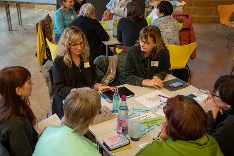 Foto: Mehrere Personen sitzen um einen Tisch und unterhalten sich.