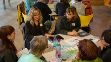 Foto: Mehrere Personen sitzen um einen Tisch und unterhalten sich.
