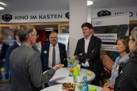 Foto: Mehrere Personen stehen um einen Tisch und unterhalten sich.