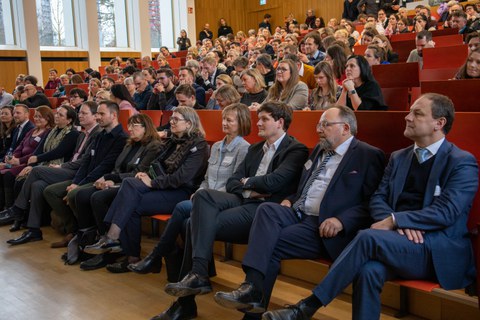 Foto: Personen in einem vollbesetzten Hörsaal blicken zur Bühne.