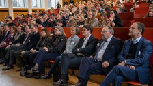 Foto: Personen in einem vollbesetzten Hörsaal blicken zur Bühne.