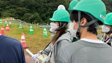 Eine Gruppe von Studierenden an einem abgesperrten Gebiet. Die Studierenden haben grüne Bauhelme auf.