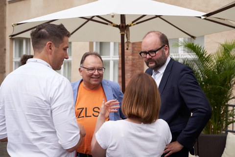 Vier Personen unterhalten sich stehend im Kreis, drei Männer, eine Frau