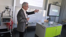 Bild, auf dem Prof. Dr. Körndle vor einer Tafel steht und einen Vortrag hält. Über der Tafel wird eine Präsentation an die Wand projiziert. Rechts im Bild sieht man eine aktive digitale Tafel.