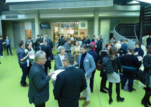 Bild des Foyers der Fakultät Informatik an der TU Dresden. Zu sehen sind mehrere Personen, die um Stehtische herum gruppiert sind und sich augenscheinlich unterhalten. Im Hintergrund ist das Studentencafé ASCII zu sehen.