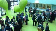Bild des Foyers der Fakultät Informatik an der TU Dresden. Zu sehen sind mehrere Personen, die teilweise um Stehtische herum gruppiert sind und sich augenscheinlich unterhalten. 