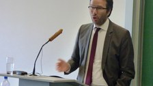 Bild, auf dem Prof. Dr. Krauthäuser, Prorektor für Bildung und Internationales vor einem Pult mit Mikrofon steht und augenscheinlich einen Vortrag hält.