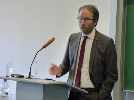 Bild, auf dem Prof. Dr. Krauthäuser, Prorektor für Bildung und Internationales vor einem Pult mit Mikrofon steht und augenscheinlich einen Vortrag hält.