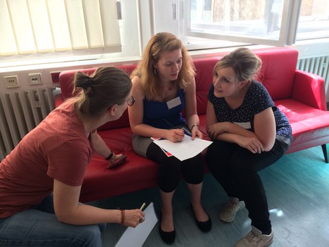 Bild von 3 Frauen, die auf einem roten Sofa sitzen und miteinander reden.