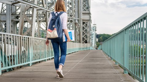 Eine Studentin hält Lernmaterial in der Hand und läuft über das Blaue Wunder.