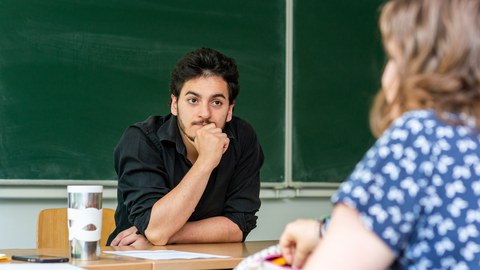 Foto: Ein Mann und eine Frau sitzen sich an einem Tisch gegenüber. Er hört ihr zu.