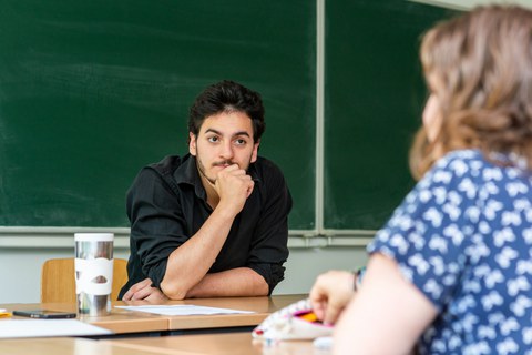 Foto: Ein Mann und eine Frau sitzen sich an einem Tisch gegenüber. Er hört ihr zu.