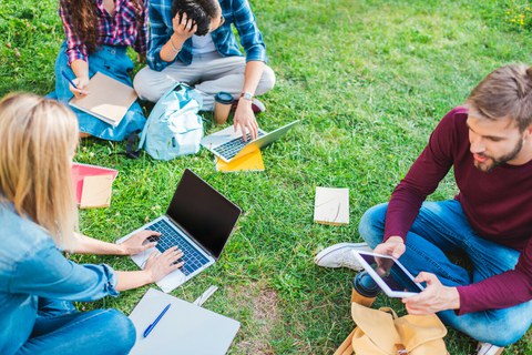 Das Foto zeigt mehrere Studierende. Sie sitzen mit ihren Laptops auf einer Wiese und lernen.